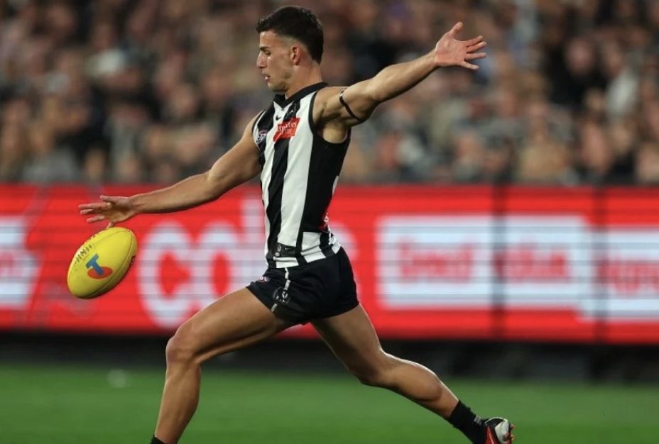 A Collingwood player drives the ball forward by foot